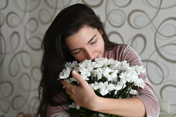 Girl rejoices over a bouquet of white flowers. Brunette hugs sniffs a bouquet of delicate flowers from her beloved. A good gift for your beloved half.