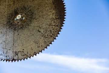 An old rustic saw wheel hanging against the clear sky. Extreme close-up view. Vintage industrial agriculture wheel. Copy space