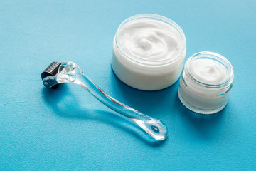 Dermaroller for home cosmetologic procedure near creams on blue background