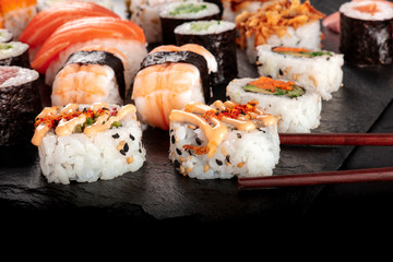 Large sushi set, close-up with chopsticks and copy space on a black background. An assortment of various maki, nigiri and rolls