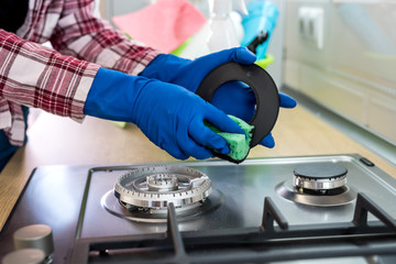 Woman with sponge and rubber protective glove used to wipe down an oven range top.