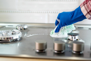 Woman with sponge and rubber protective glove used to wipe down an oven range top.