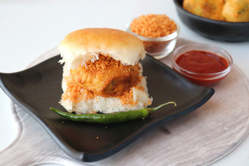 Vada pav or wada pao is a vegetarian fast food dish native to the state of Maharashtra. Famous Mumbai street food served with Red chutney and fried green chili. Copy space