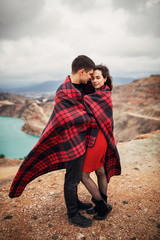 loving couple a young man and a girl wrapped themselves in a red-black plaid and gently cuddle in their hands a caramel on a stick on a background of a heart-shaped lake in softfocus
