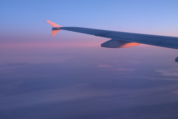 Airplane wing through the porthole in the rays of the setting sun in blue and pink colors