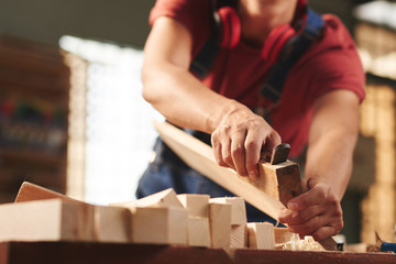 Low angle view of unrecognizable professional carpenter carefully smoothing wooden plank with hand plane