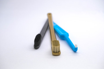 Three colored  toothbrushes gold, black and blue for different purposes on a light background