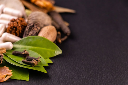 Extreme close up of cloves and green leaves with blurred capsules in the black background. Herbal concept