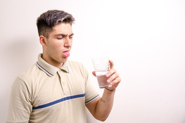 Young man with a glass of water in his hand looking disgusted