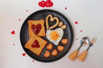 Healthy Love Breakfast on Valentine's Day - fried eggs and brown bread in the shape of a heart, chicken sausages and sweet biscuits. Top view with copy pace. Valentines day greeting.