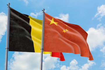 China and Belgium flags waving in the wind against white cloudy blue sky together. Diplomacy concept, international relations.