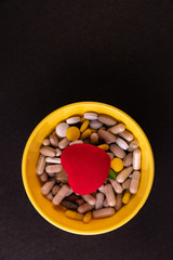 Herbal medicine concept. Top view of herbal medicines with red heart in a bowl with a black background