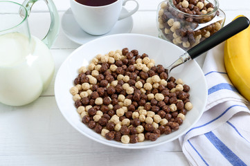 Wholegrain chocolate and milk balls, fruit, tea and milk on white wooden background. Healthy cereal breakfast. Baby breakfast. Baby eating. Balanced diet.