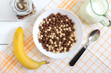 Wholegrain chocolate and milk balls, fruit and milk on white wooden background. Healthy cereal breakfast. Baby breakfast. Baby eating. Balanced diet