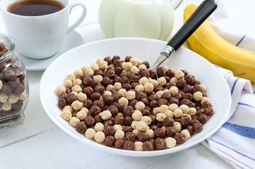 Wholegrain chocolate and milk balls, fruit, tea and milk on white wooden background. Healthy cereal breakfast. Baby breakfast. Baby eating. Balanced diet.