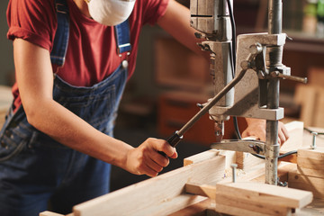 Close-up view of female carpenter in denim overall pressing lever on woodworking machine while processing wooden planks - obrazy, fototapety, plakaty