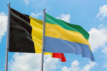 Gabon and Belgium flags waving in the wind against white cloudy blue sky together. Diplomacy...
