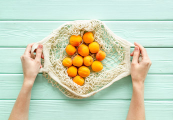 Eco shopping. Textile bag with fruits in hands on green wooden background top-down