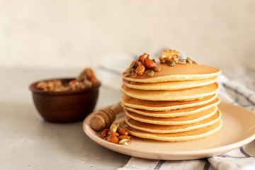 Stack of delicious pancakes with chocolate, honey, nuts and slices of banana on plate and napkin on wooden background