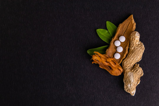 Top view mid close up of dried ginger, cinnamon stick, javitri and four white herbal pills on a copy space black balcground
