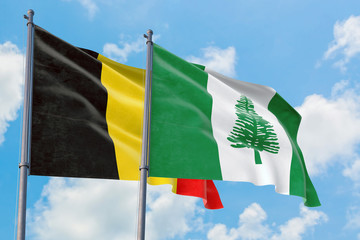 Norfolk Island and Belgium flags waving in the wind against white cloudy blue sky together. Diplomacy concept, international relations.