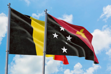 Papua New Guinea and Belgium flags waving in the wind against white cloudy blue sky together. Diplomacy concept, international relations.