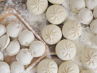 top view on wooden table with homemade food. hand made raw dumplings on wooden dish and rolling pin covered with flour