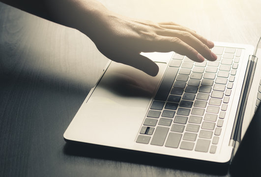 Man Hand Using Laptop On Black Desk With Blur Background And Light Flare