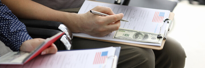 Close-up view of people filling usa visa application forms with personal passports at embassy....
