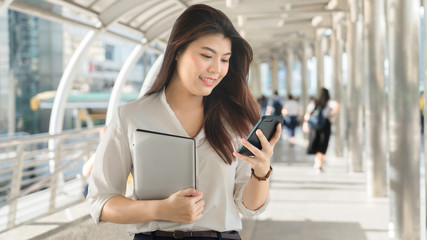 Business woman smiling holding laptop use smartphone working to outdoor city.