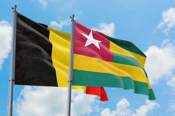 Togo and Belgium flags waving in the wind against white cloudy blue sky together. Diplomacy concept, international relations.
