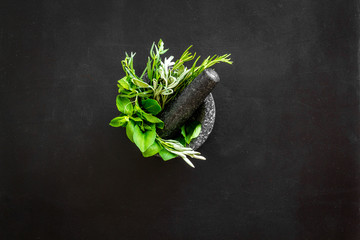 Herbs in ceramic mortar with pestle on black backgroud top-down copy space