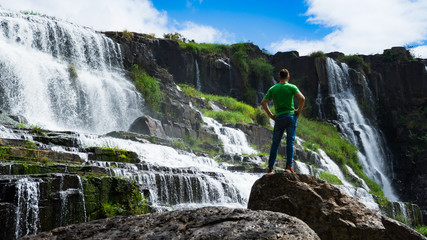 Young men staying near amazing  waterfall in Da Lat city Vietnam.Traveler boy with long red hair looking to beautiful Pongour  waterfall.