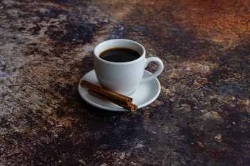 White cup of coffee with a saucer with cinnamon sticks on a dark background with place for text top view