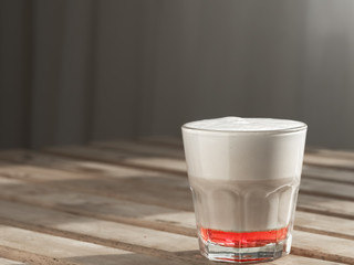 Hot coffee cappuccino with raspberry syrup in glass with milk foam on wooden table. Shallow depth of field, focus on the cup. Close up. Copy space.