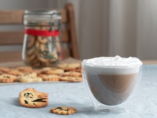Hot coffee cappuccino in glass with milk foam and crackers on wooden table. Close up. Copy space. Shallow depth of field, focus on the cup.