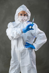 Doctor in a white medical protective suit on a gray background stands in front of the camera in various poses.