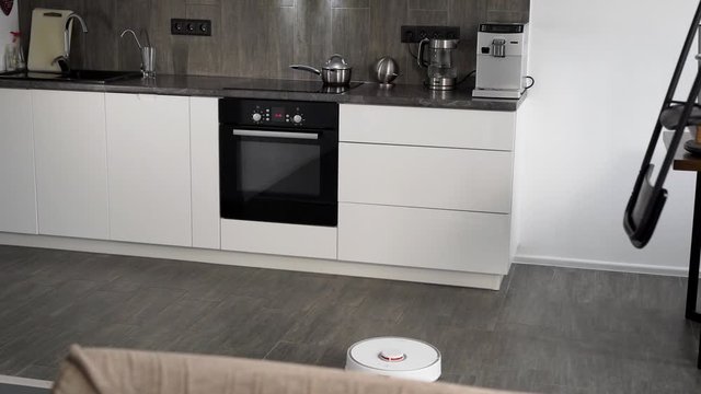 In a stylish modern kitchen is cleaning. The automatic robot vacuum cleaner moves along its trajectory. Elements of a smart home make life easier for people