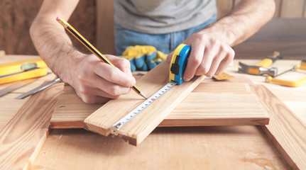 Carpenter measuring wooden plank and making marks with a pencil.