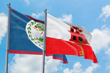 Gibraltar and Belize flags waving in the wind against white cloudy blue sky together. Diplomacy...