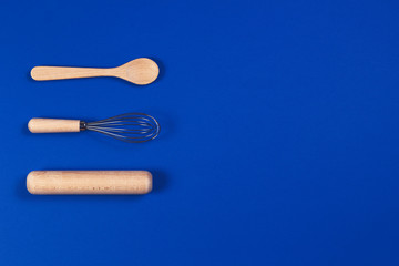 Bakeware. Wooden spoon, rolling pin and balloon whisk on blue background. Top view, flat lay