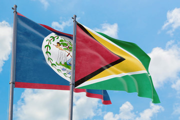Guyana and Belize flags waving in the wind against white cloudy blue sky together. Diplomacy concept, international relations.