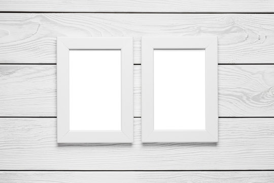 Two white empty frames hanging on the white wooden wall