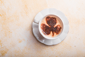 Top view of coffee cup with four leaf clover latte art on light  background.