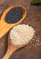 White and black sesame seeds in  spoons on wooden  background, top view, close up