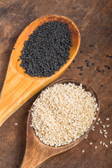 White and black sesame seeds in  spoons on wooden  background, top view, close up