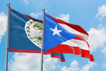 Puerto Rico and Belize flags waving in the wind against white cloudy blue sky together. Diplomacy concept, international relations.