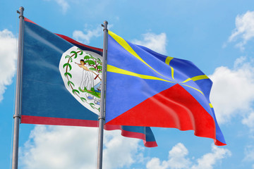 Reunion and Belize flags waving in the wind against white cloudy blue sky together. Diplomacy concept, international relations.