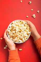 Popcorn viewed from above on red background. Child eating popcorn. Human hand.  Cinema snack concept. The food for watching a movie and entertainment. Copy space for text, flat lay.