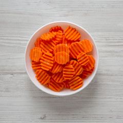 Fresh Raw Organic Carrot Chips in a white bowl over white wooden background, top view. From above, overhead, flat lay. Close-up.